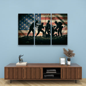 A three-panel canvas wall art set depicting the silhouette of soldiers carrying a flag across a battlefield, set against a blue wall above a wooden console table with decorative items.