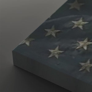 A close-up of a rectangular canvas or panel featuring a dark blue background with raised white stars, photographed on a dark gray surface.