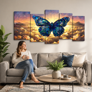 A woman sits on a gray sofa in a living room, holding a mug and looking at a five-panel canvas wall art set depicting a large blue butterfly over a golden sunset sky with clouds.
