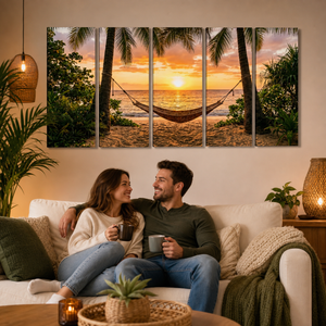 A four-panel canvas wall art set depicting a tropical beach sunset with palm trees and a hammock, displayed on a beige wall above a couple sitting on a white sofa in a cozy living room.