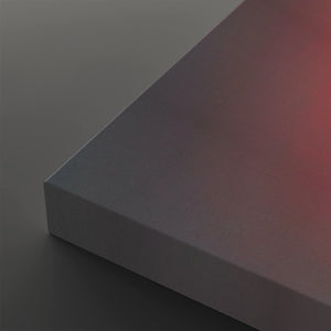 A close-up of a rectangular panel or block with a smooth gradient surface shifting from dark gray to muted pink, resting on a dark gray surface.