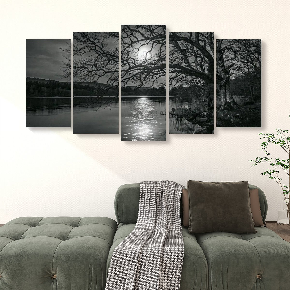 A five-panel black and white canvas wall art set depicting a moonlit lake scene with bare trees, shown hanging above a green sofa in a living room setting.
