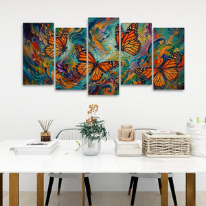 A five-panel canvas wall art set depicting vibrant orange monarch butterflies over colorful swirling abstract backgrounds, displayed on a white wall above a styled dining table with books, a vase, and a basket.
