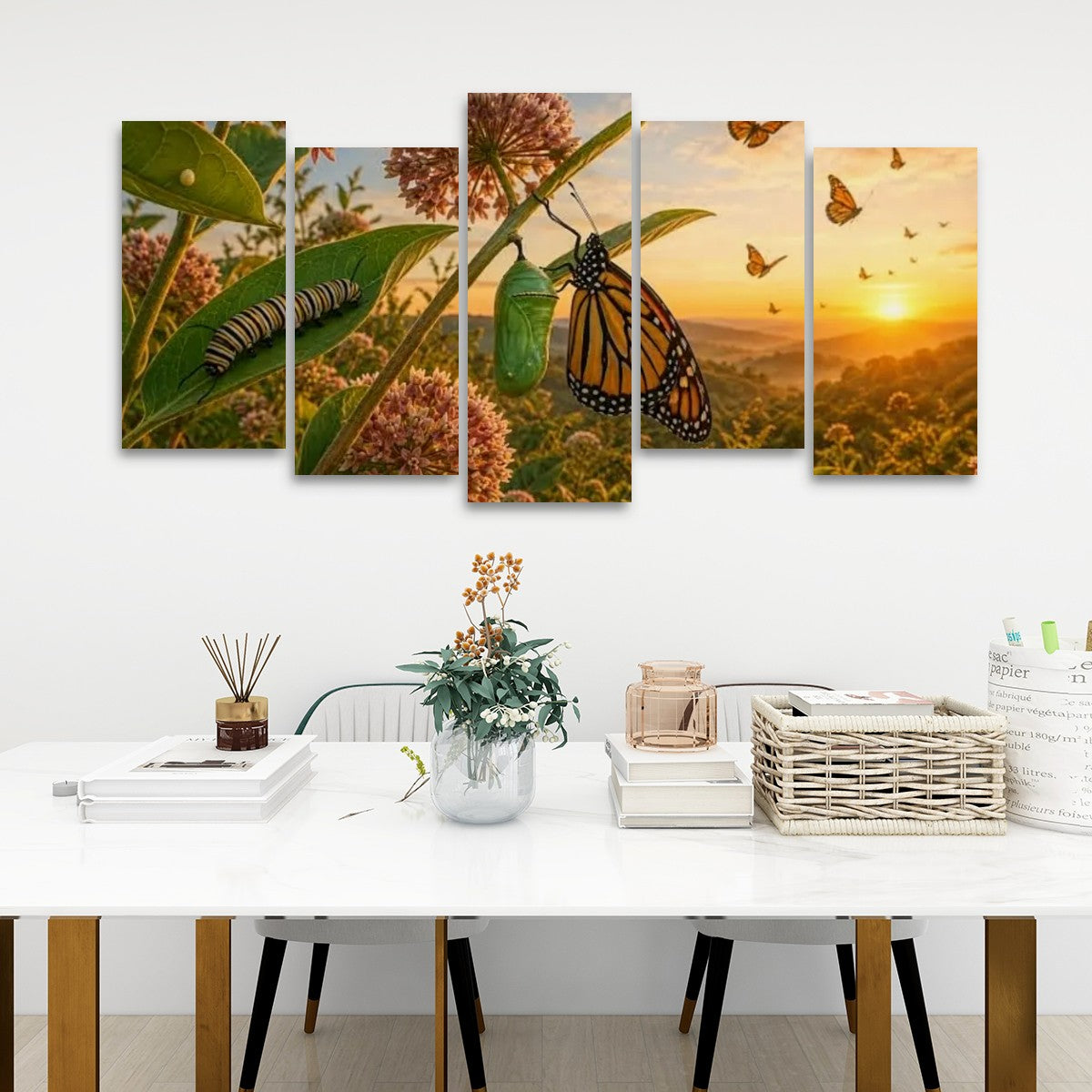 A five-panel canvas wall art set depicting butterflies, a monarch caterpillar, a green chrysalis, and a golden sunset landscape, displayed on a white wall above a styled dining table.