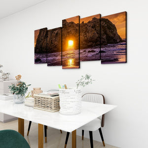 A 5-panel canvas wall art set depicting a dramatic rocky coastline at sunset, displayed on a white wall above a dining table in a modern room setting.