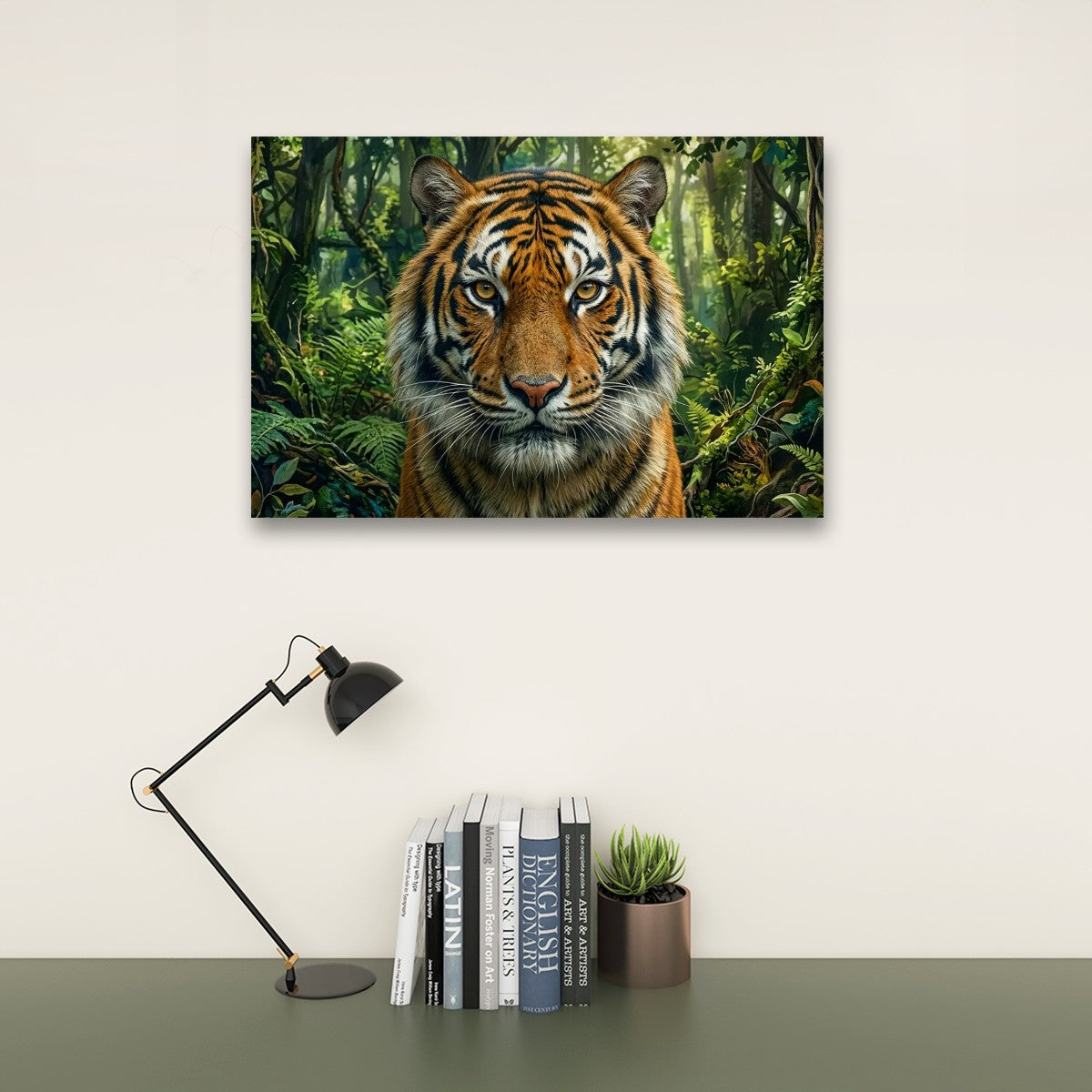 A rectangular wall art print showing a close-up tiger in a lush green jungle, displayed above a desk with a black lamp, books, and a small succulent on a light beige wall.