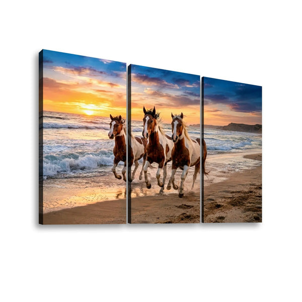 Three-panel canvas wall art showing three horses running on a beach at sunset, displayed against a plain white background.