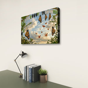A rectangular wall art print showing monarch butterflies flying among green leaves against a cloudy sky, displayed on a white wall above a desk with books, a lamp, and a small plant.