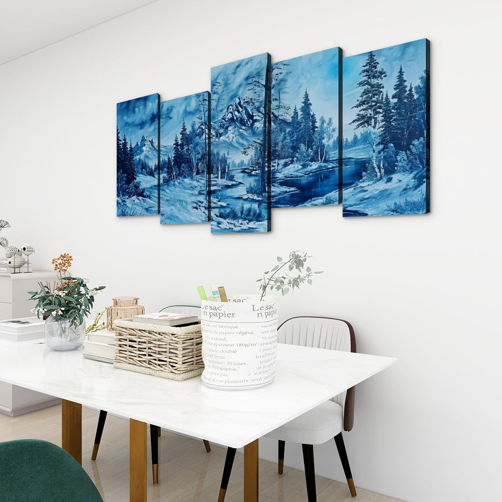 A five-panel canvas wall art set depicting a snowy mountain landscape with pine trees and blue water, displayed above a white dining table in a modern room setting.
