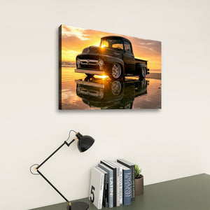 A rectangular wall art print showing a vintage black  1956 Ford  F-100 pickup truck on a beach at sunset, mounted on a light wall above a desk with a black lamp and books.