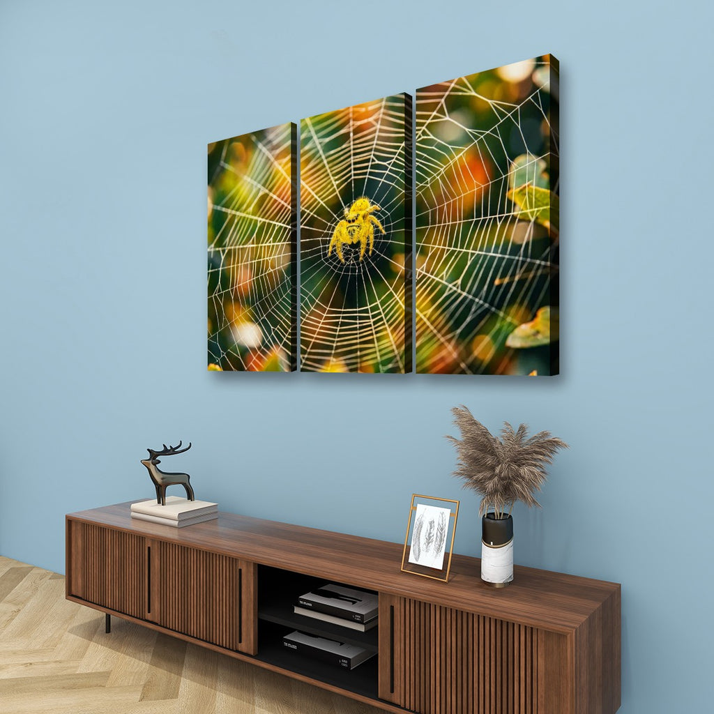Three-panel canvas wall art depicting a yellow spider on a detailed web, displayed on a light blue wall above a wooden console table with decorative items.