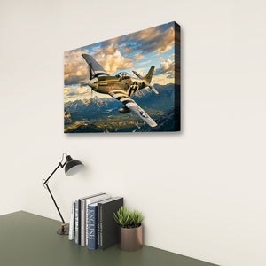 A rectangular wall art print or canvas showing a vintage military fighter plane flying over mountains under a dramatic cloudy sky, displayed on a light wall above a desk with books, a lamp, and a small plant.