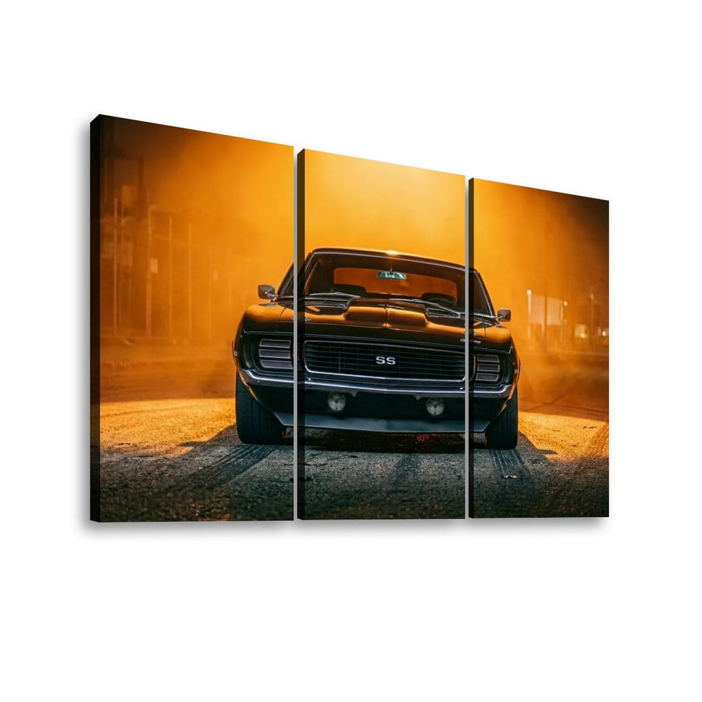 A three-panel canvas wall art print showing a black 1969 RS/SS Chevy Camaro muscle car facing forward on a road with dramatic orange-yellow haze and smoke. The artwork is presented as a multi-panel print against a plain white background.