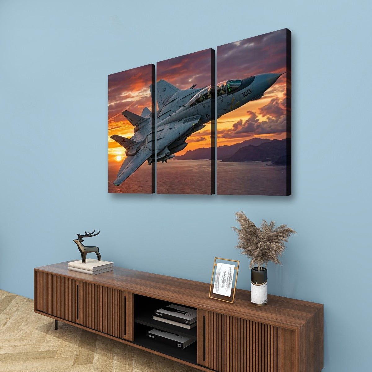 A three-panel canvas wall art set depicting a gray Grumman F-14 Tomcat military fighter jet flying over a sunset landscape, displayed on a light blue wall above a wooden console table with decorative items.