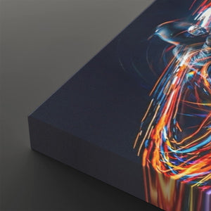 A close-up of a rectangular canvas or print showing an abstract dark scene with vivid streaks of orange, yellow, blue, and white light on the right side, photographed against a dark gray background.