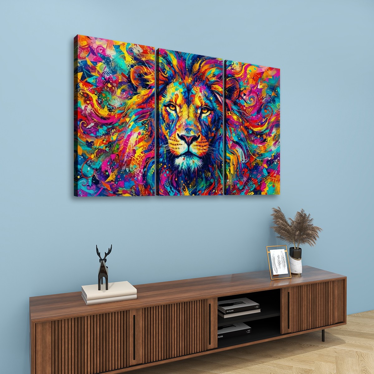 A three-panel canvas wall art set depicting a colorful, vibrant painted lion portrait, displayed on a light blue wall above a wooden console table with decorative items.