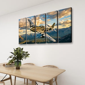 A four-panel canvas wall art set depicting a vintage military airplane flying over mountains under a dramatic cloudy sky, displayed on a white wall above a dining table with chairs and a plant.