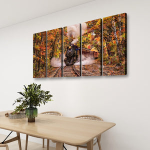 A four-panel canvas wall art set depicting an autumn forest scene with a steam train, displayed on a white wall above a light wood dining table with chairs and a potted plant.