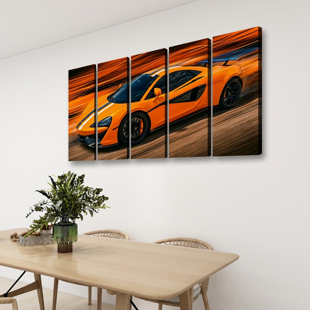 A four-panel canvas wall art print depicting a bright orange sports car in motion, displayed on a white wall above a light wood dining table with chairs and a green plant.