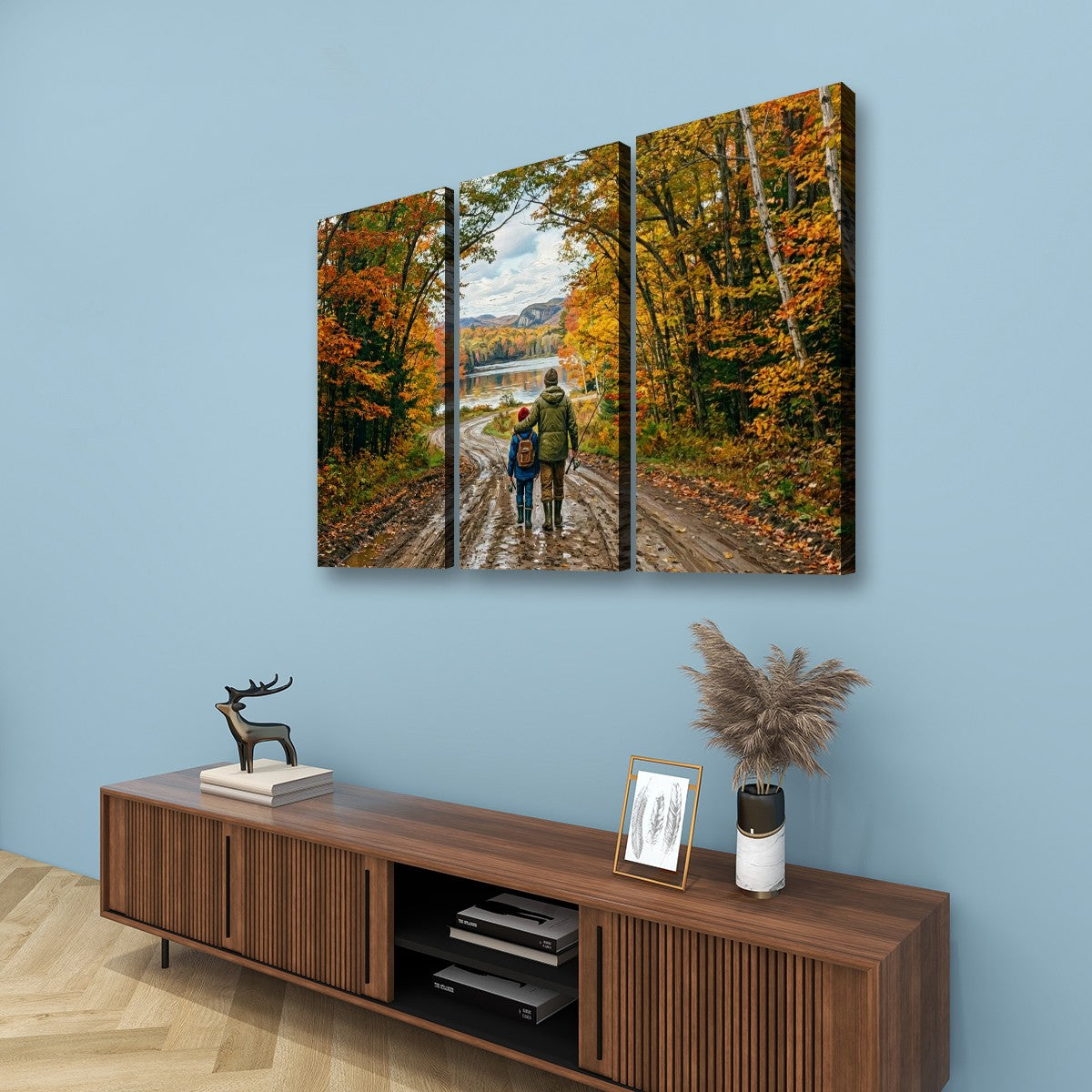 Three-panel canvas wall art depicting a couple walking on a dirt road through an autumn forest, displayed on a light blue wall above a wooden console table with decorative items.