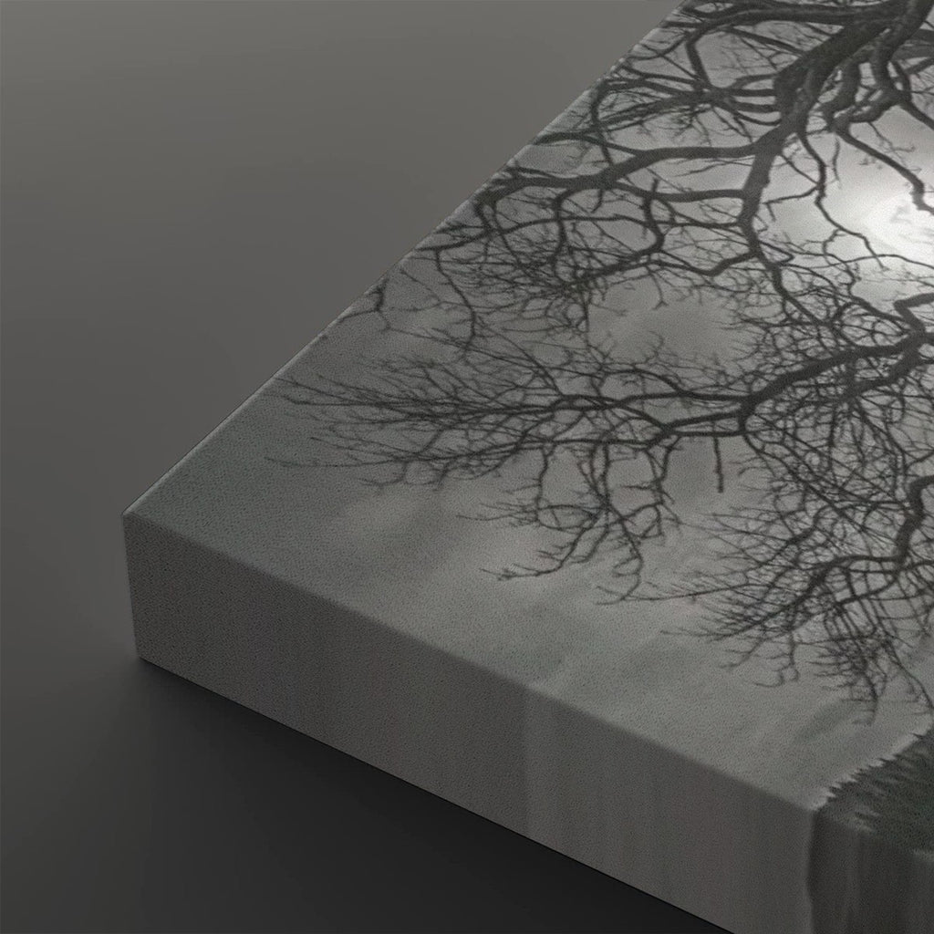 A close-up of a rectangular canvas print showing a black-and-white tree branch pattern against a pale sky-like background, photographed on a dark gray surface.