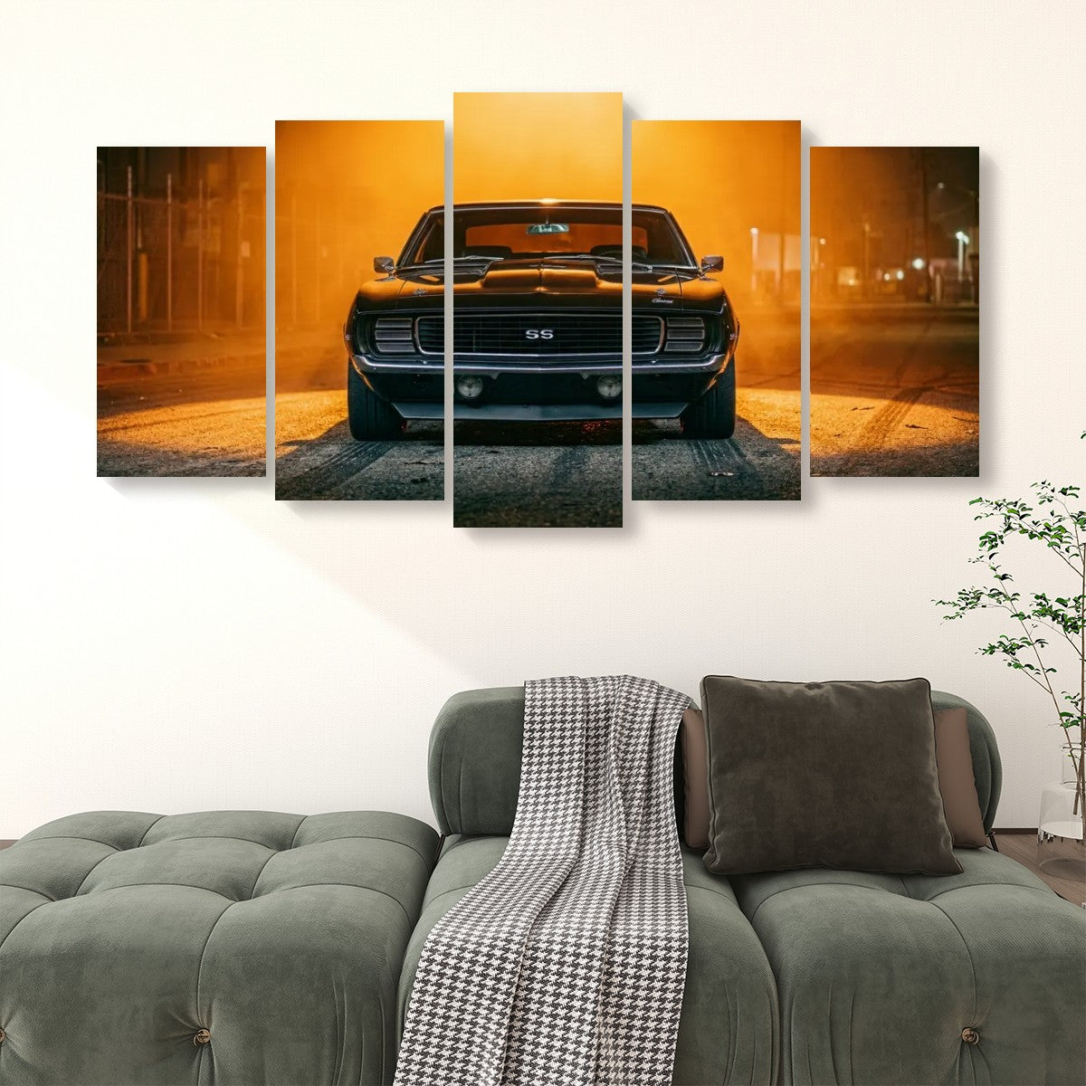 A five-panel canvas wall art set depicting a black 1969 RS/SS Chevy Camaro muscle car in a dramatic orange-lit street scene, displayed above a green tufted sofa in a modern living room setting.