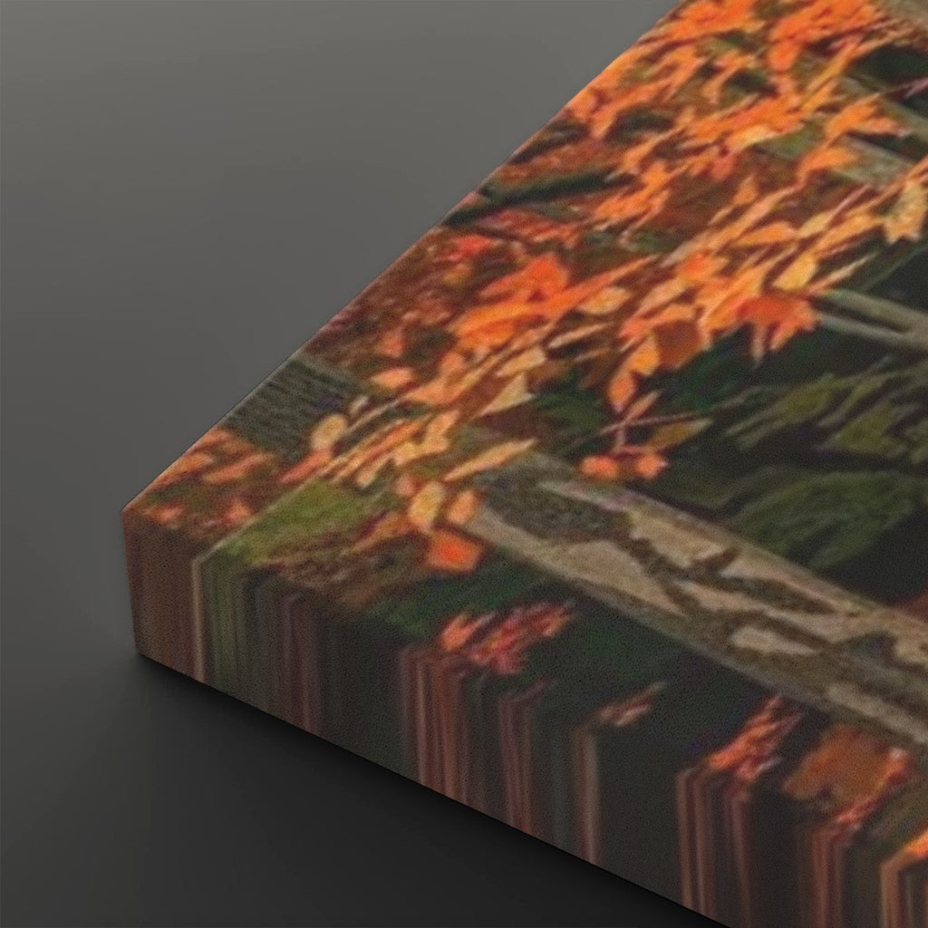 A close-up of a rectangular canvas or print showing an autumn forest scene with orange and yellow leaves over dark green and brown branches, photographed on a dark gray background.