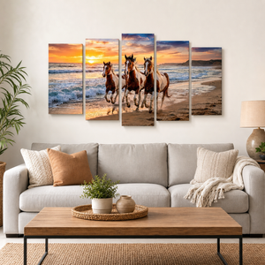 A 5-panel canvas wall art set depicting three horses running through ocean waves at sunset, displayed on a wall above a light gray sofa in a modern living room setting.