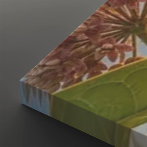 A close-up angled view of a rectangular canvas or print showing a floral design with pink-brown blossoms and a large green leaf, photographed against a dark gray background.