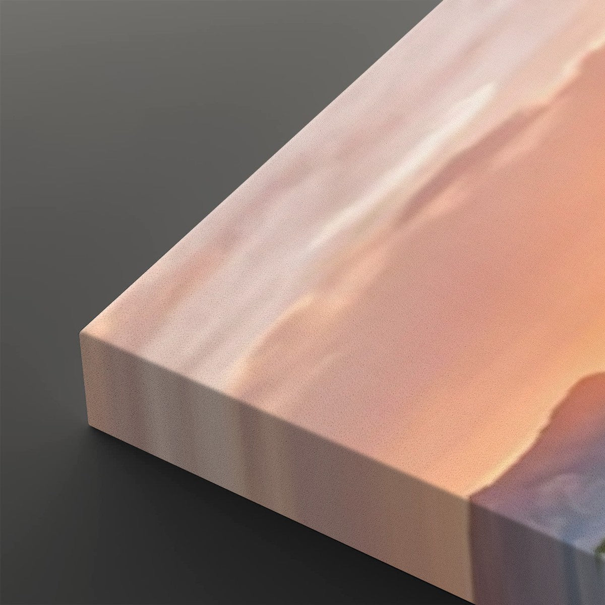 A close-up of a rectangular canvas or panel with a soft abstract landscape print in peach, pink, cream, and muted blue tones, shown against a dark gray background.