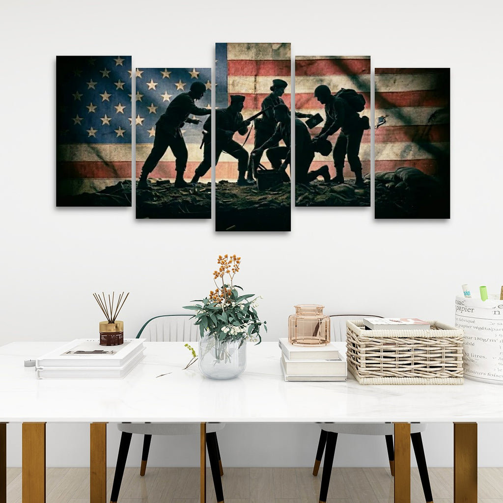 A five-panel canvas wall art set depicting the silhouette of five soldiers carrying a wounded comrade against a distressed American flag background, displayed on a white wall above a modern white dining table.