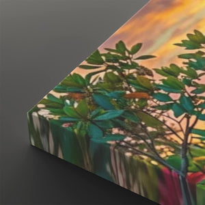A close-up of a canvas or print showing a botanical scene with green leaves and branches against a warm orange and yellow sky, photographed on a dark gray background.