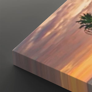 A close-up of a rectangular canvas or panel showing a warm-toned abstract landscape print with peach, pink, orange, and yellow hues, photographed on a dark gray background.
