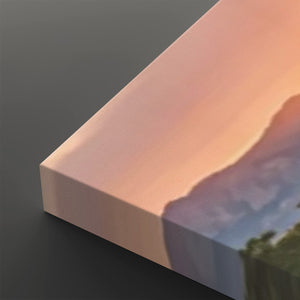 A close-up of a rectangular canvas or print block showing a soft sunset landscape with peach, pink, and blue tones, photographed on a dark gray background.