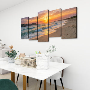 A 4-panel canvas wall art set depicting a beach sunset with ocean waves, displayed on a white wall above a dining table in a modern room setting.