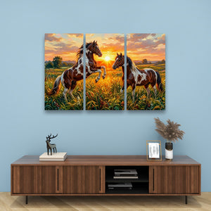 A three-panel canvas wall art set depicting two brown and white horses in a golden field at sunset, displayed on a light blue wall above a wooden console table with decorative items.
