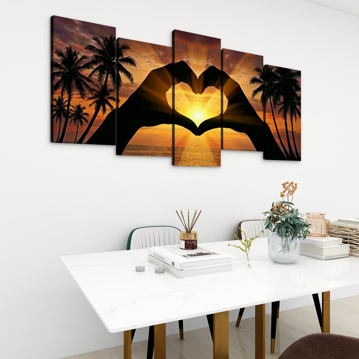 A 5-panel canvas wall art set depicting a sunset with palm tree silhouettes and two hands forming a heart shape, displayed on a white wall above a dining table in a modern room setting.