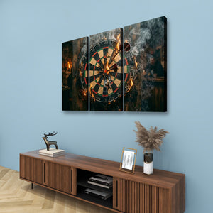 A three-panel canvas wall art set depicting a burning dartboard with smoke and warm light, displayed above a wooden console table against a light blue wall.