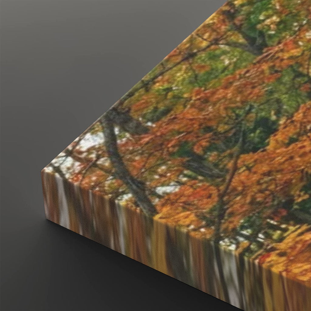 A rectangular canvas or print showing an autumn forest scene with orange and yellow leaves, green foliage, and tree branches, photographed at an angle on a dark gray background.