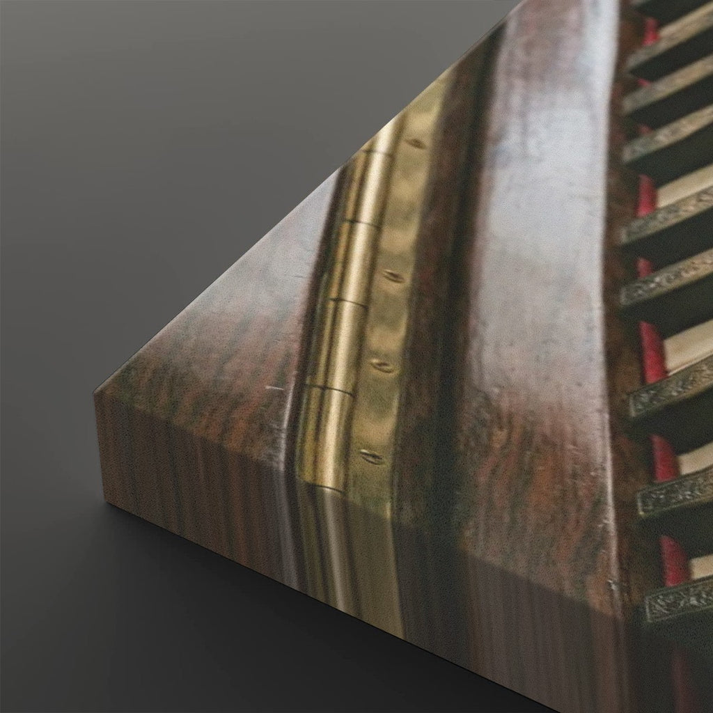 Close-up of a wooden stringed instrument corner showing a polished brown wood grain, brass metal hardware, and part of the strings against a dark gray background.