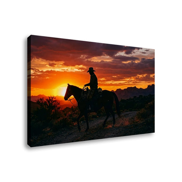 A rectangular wall art canvas showing a silhouetted cowboy riding a horse across a desert landscape at sunset, photographed against a plain white background.