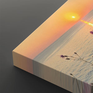A close-up of a canvas wall art print showing a sunset over water, with warm orange and yellow light blending into a pale blue and beige horizon. The canvas is photographed at an angle on a dark gray background.