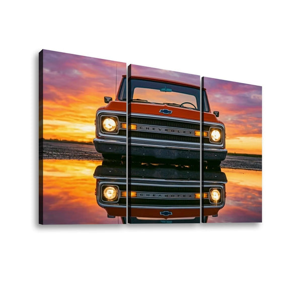 Three-panel canvas wall art showing a red Chevrolet truck at sunset with its reflection on the water, displayed against a white background.
