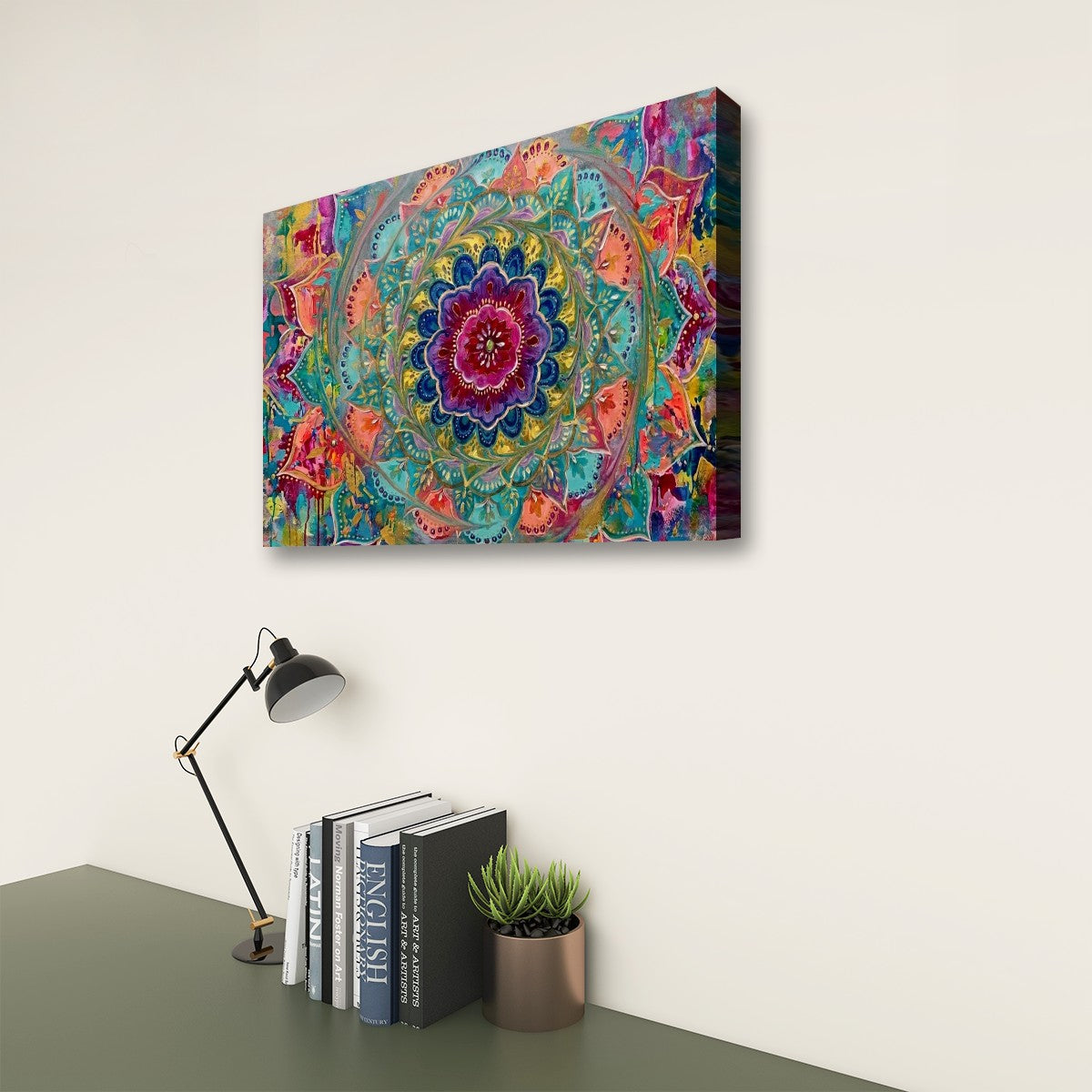 A colorful abstract mandala canvas wall art print hanging on a light beige wall above a dark green desk with a black desk lamp, books, and a small potted succulent.