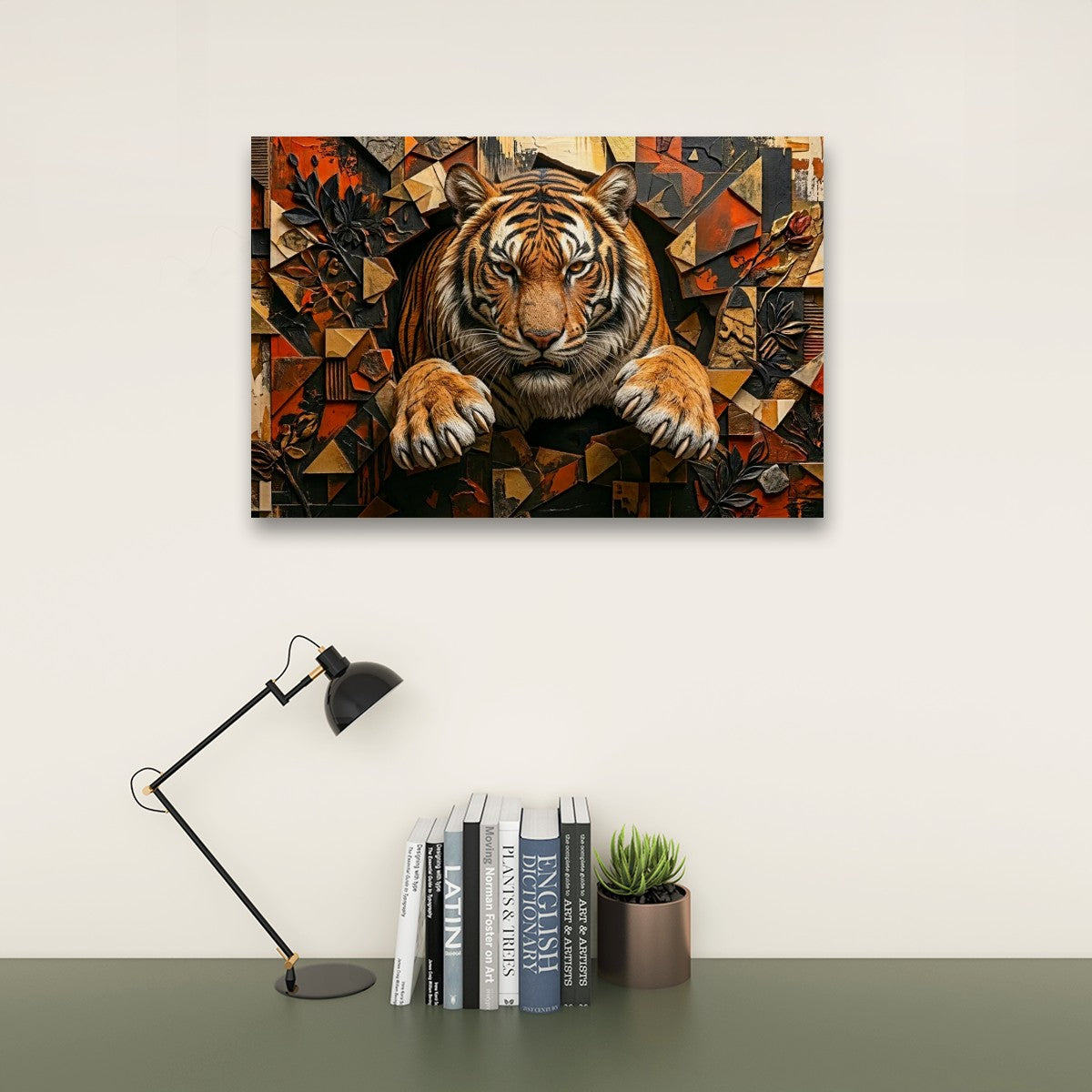 A rectangular wall art print showing a stylized tiger emerging from a geometric mosaic background, displayed above a desk with a black lamp, books, and a small succulent against an off-white wall.