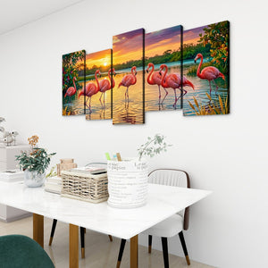 A 5-panel canvas wall art set depicting pink flamingos at sunset, displayed on a white wall above a dining table in a modern room setting.