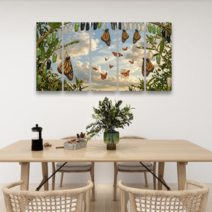 A five-panel canvas wall art print depicting monarch butterflies flying through green foliage against a cloudy sky, displayed on a white wall above a dining table with chairs.