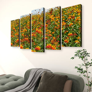 A five-panel canvas wall art set depicting a vibrant field of yellow and orange flowers with monarch butterflies, displayed on a white wall above a modern gray sofa in a living room setting.