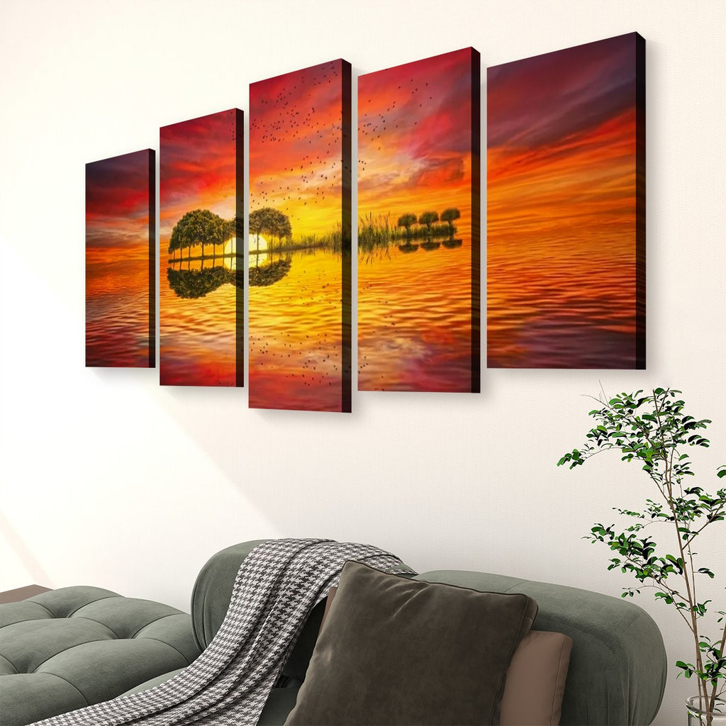 A five-panel canvas wall art set depicting a dramatic sunset over water with mirrored trees, displayed above a green sofa in a living room setting.