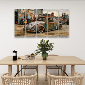 A multi-panel canvas wall art print depicting a vintage, rusted blue and green Volkswagen Beetle in a gravelly outdoor setting, displayed on a white wall above a light wood dining table with woven chairs.